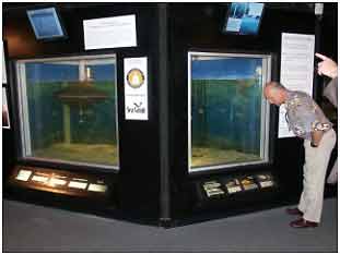 A visitor looks at the OAC exhibit showing a large-scale model of the cage, including its Robofeeder, shackles, ballast weight, and mooring system.